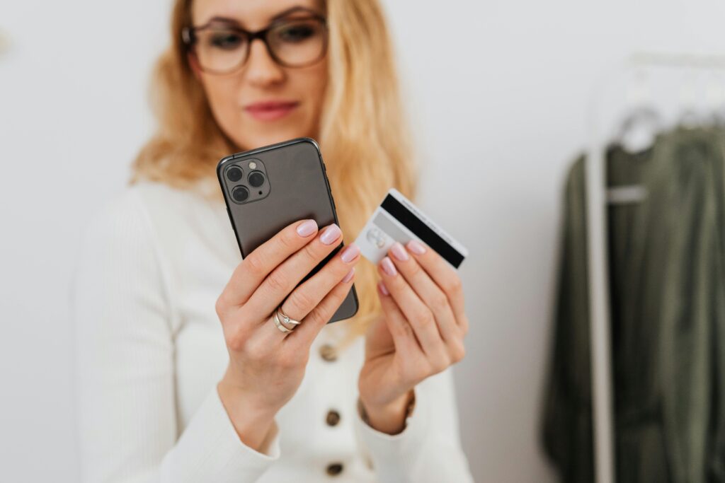 pexels-photo-5717950-5717950 A woman holding a smartphone and credit card, engaging in online shopping indoors.