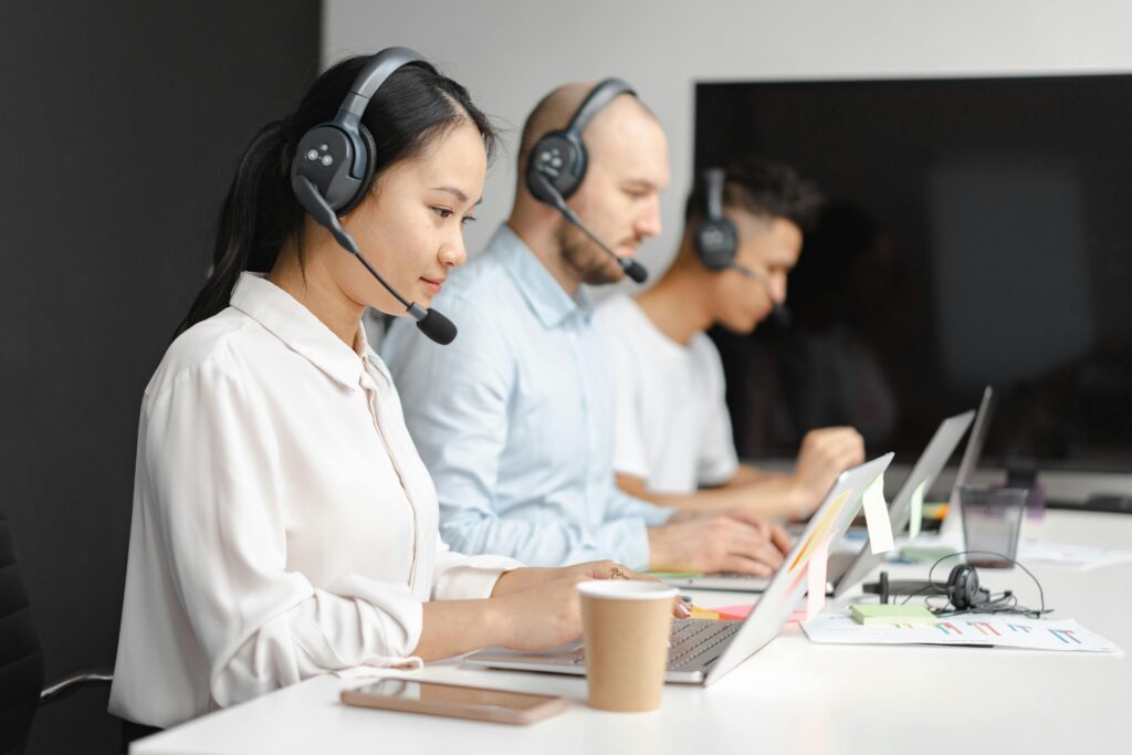 pexels-photo-7682340-7682340 Customer service agents efficiently handle calls using laptops and headsets in a modern office.