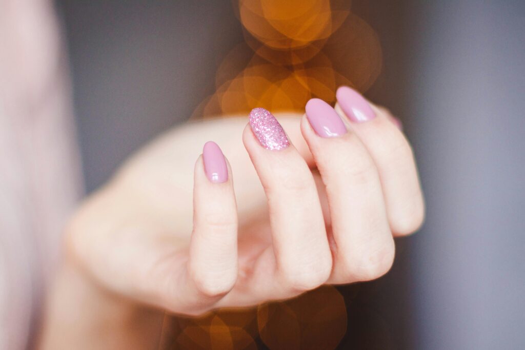 A close-up of a woman's hand displaying a stylish pink glitter manicure, highlighting nail art details.