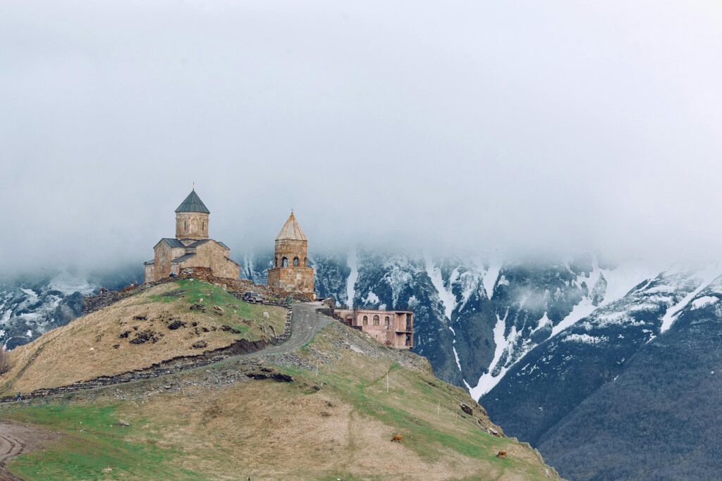 pexels-photo-4916521-4916521 Gergeti Trinity Church atop a hill, shrouded in mist against mountainous backdrop.